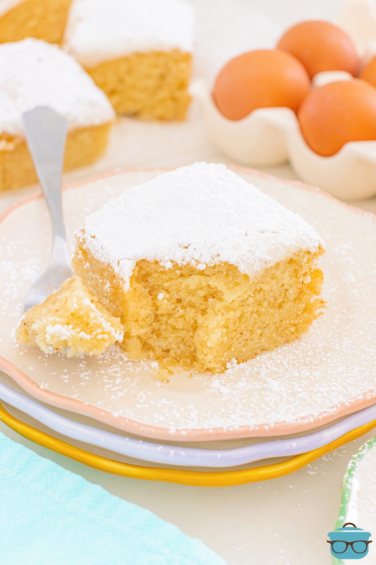 A fork holding a bite of a slice of the Powdered Sugar Donut Snack Cake next to it on a plate.