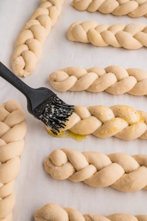 Garlic butter being brushed over the unbaked breadsticks.