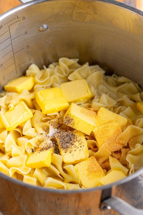 Butter, salt, and pepper being added to noodles in a pot.