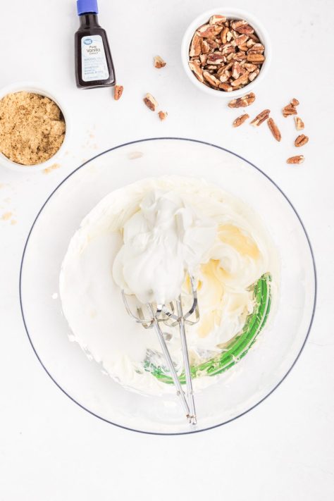 A bowl of cream cheese, sour cream, sugar, and vanilla extract mixed together.