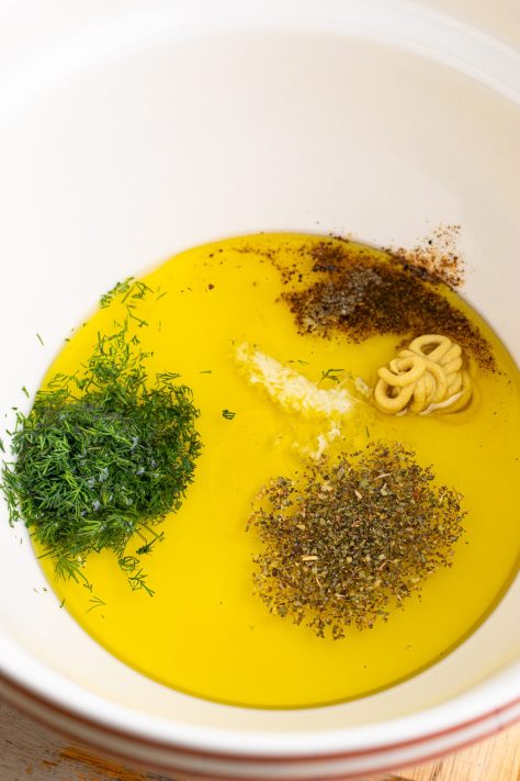 A bowl with olive oil, lemon juice, dill, sugar, garlic, oregano, salt, and pepper.