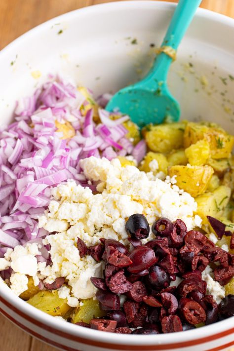 Red onion, feta, and olives being added to potatoes.