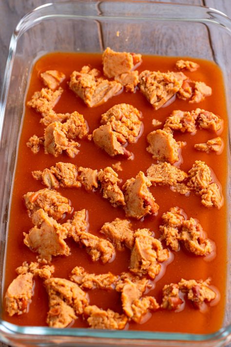 Dollops of refried beans in enchilada sauce in a baking dish.