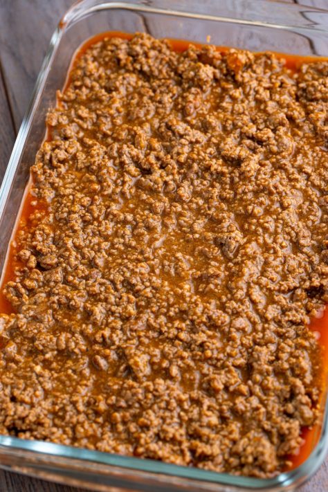 Meat mixture on top of enchilada sauce with refried beans in a baking dish.