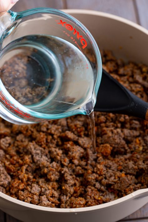 Water being added to a skillet of ground beef.