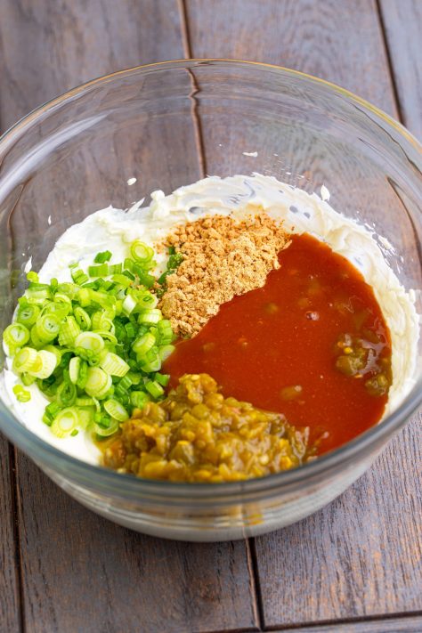 A bowl of cream cheese, taco seasoning, remaining enchilada sauce, half of the Colby Jack cheese, green onions, and green chiles.