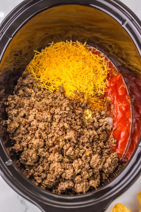 A slow cooker with salt, pepper, chili seasoning, garlic, diced tomatoes with green chilies, tomato sauce and half cup of cheese.