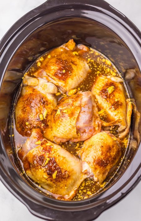 Browned chicken thighs and a sauce in a Slow Cooker.