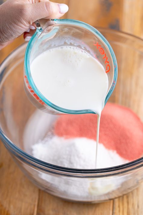 Milk, strawberry jello mix, and pudding mix in a bowl.