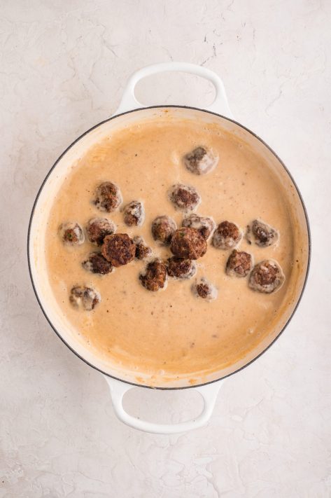 A homemade cream sauce in a pan with meatballs.