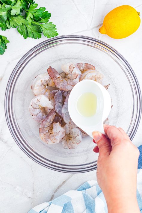 Oil being drizzled over shrimp in a bowl.