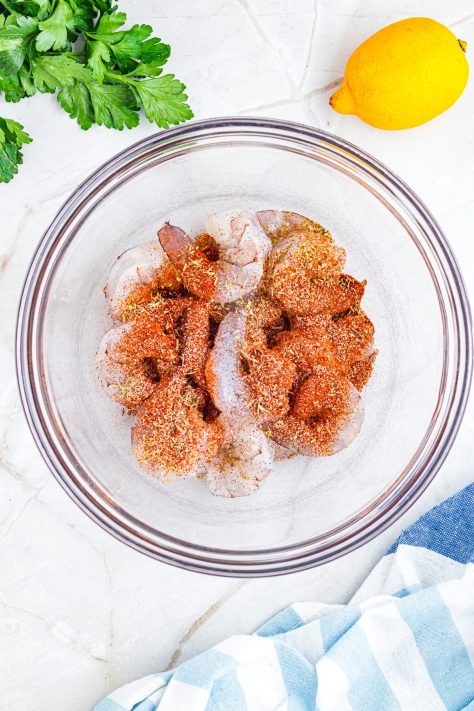 Seasonings on top of shrimp in a bowl.
