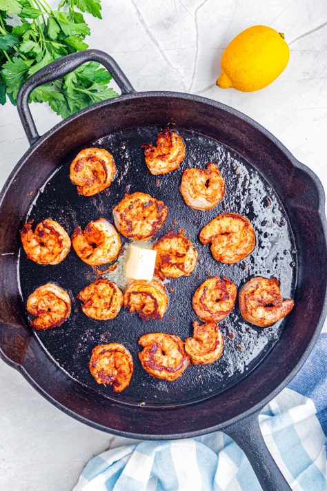 Butter being added to a skillet with shrimp cooking.