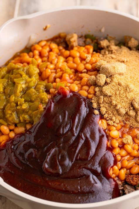 Beans, seasonings and more added to beef, and veggies in a pan.