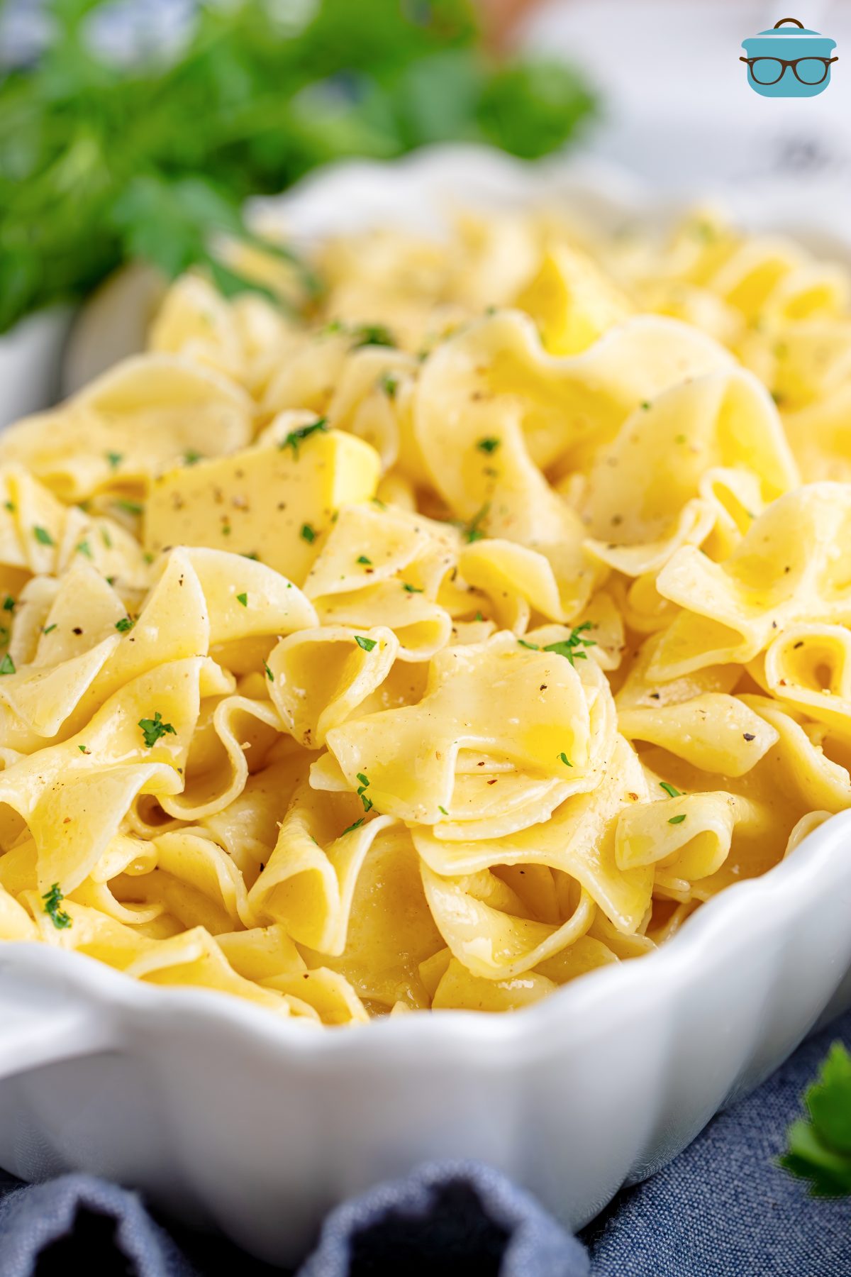 A baking dish with Buttered Noodles and a serving spoon stirring them.