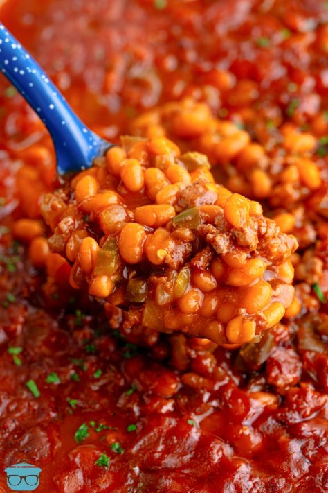 A blue serving spoon getting a scoop of Cowboy Baked Beans from the pot.
