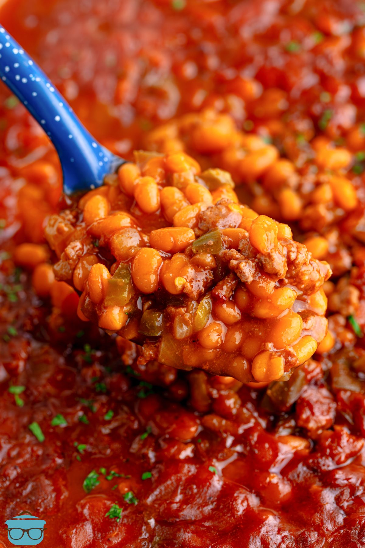 A blue serving spoon getting a scoop of Cowboy Baked Beans from the pot. 