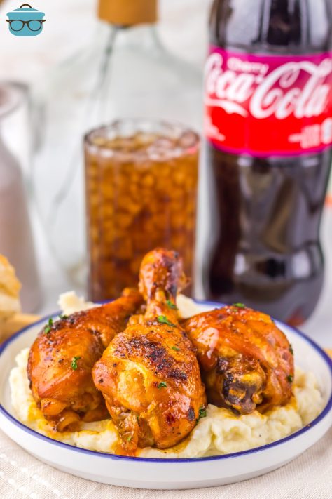 A plate of three Crock Pot Cherry Cola Drumsticks with a soda bottle and a glass of coke.