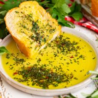 A serving plate of Carrabbas Herb Dipping Oil with a slice of bread.