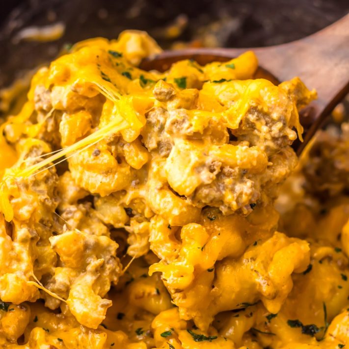 A wooden serving utensil stirring a scoop of Crock Pot Cheeseburger Helper.
