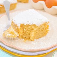 A dessert plate with a slice of Powdered Sugar Donut Cake and a fork holding a bite of it.