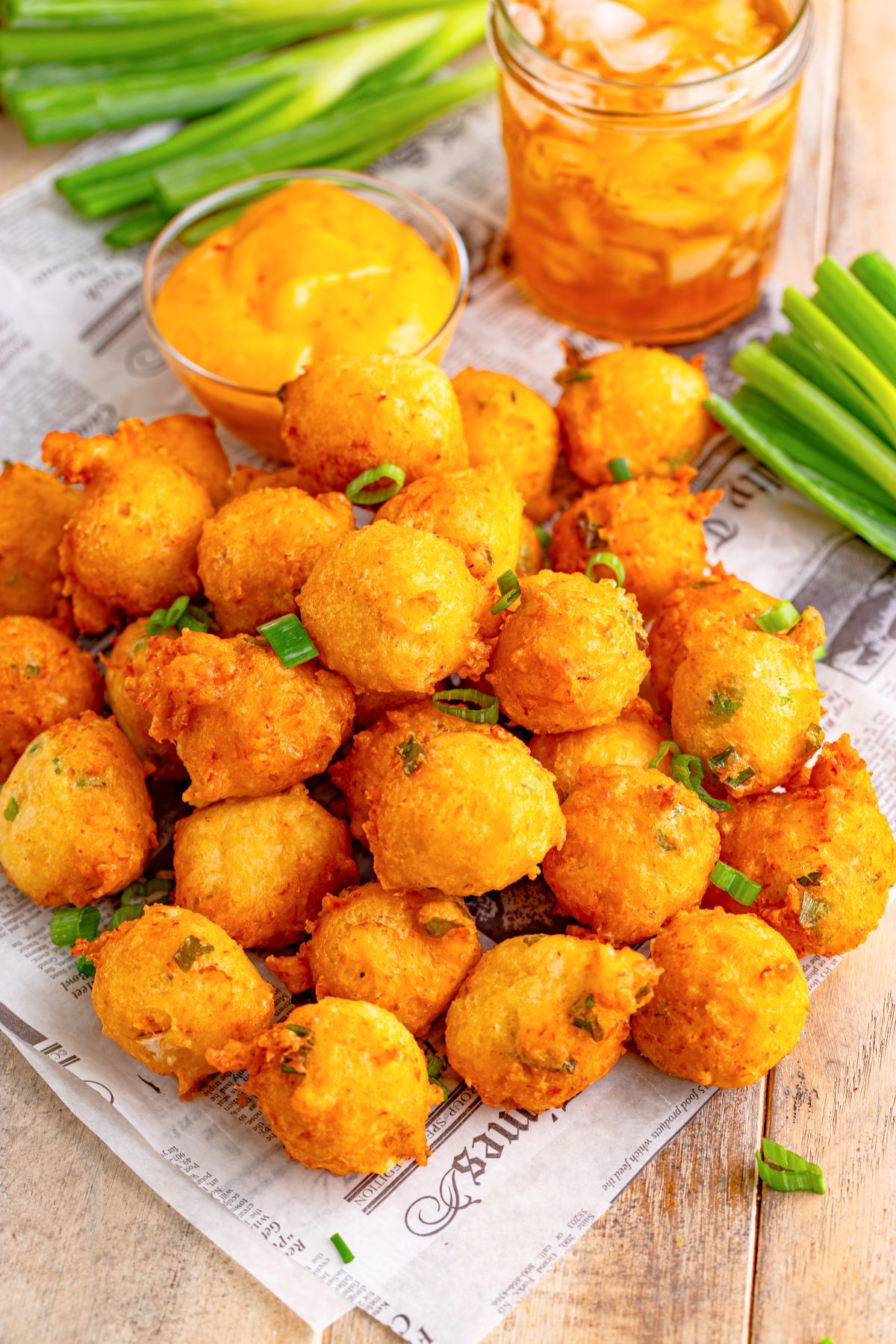 A large pile of Shrimp Fritters with a glass of tea.