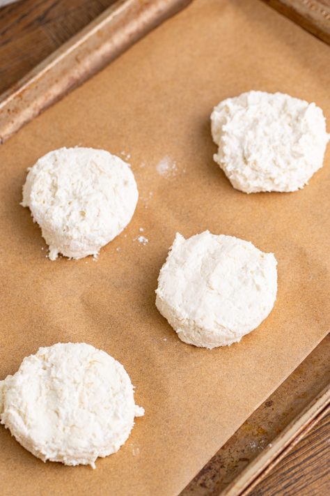Raw biscuit dough pieces on a lined baking sheet.