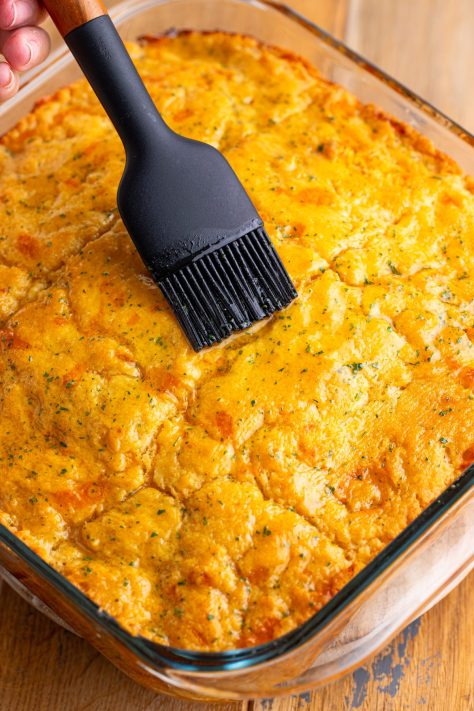 A pastry brush spreading butter and seasoning mixture over baked biscuits.
