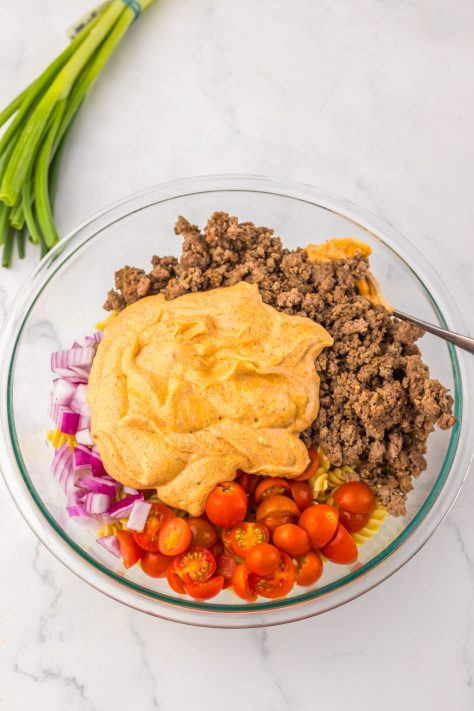 A Cool Ranch Taco Pasta Salad being added to a bowl to be mixed.