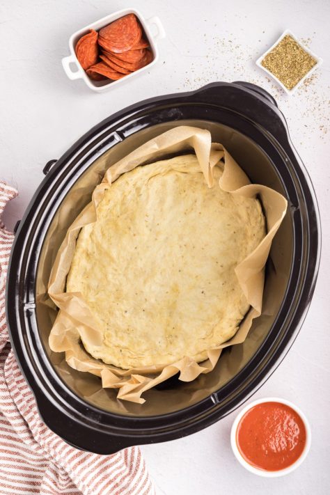 Pizza dough spread out in a lined Crock Pot.