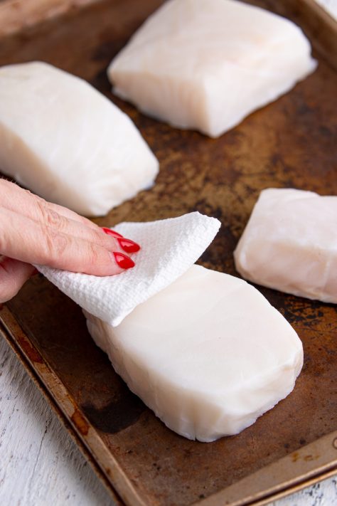 A hand patting sea bass filets dry with paper towels.