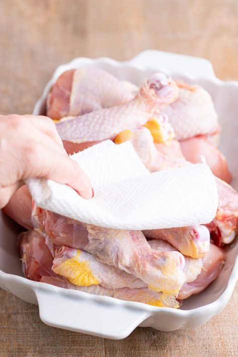 A hand using a paper towel to pat chicken legs dry.