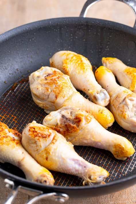 Chicken legs being seared in a pan.