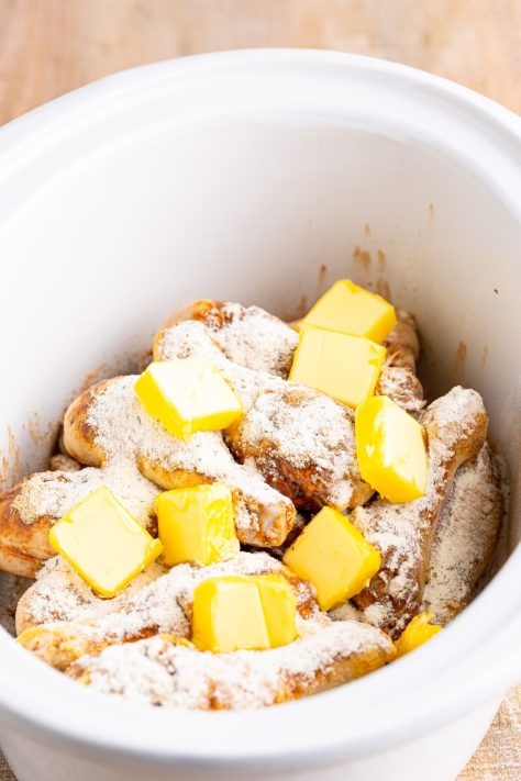 Butter and seasonings on chicken legs in a Crock Pot.