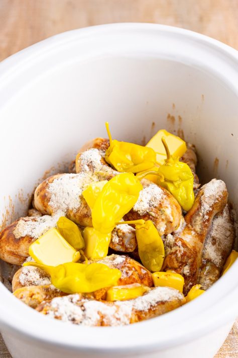 Peppers, butter, and seasonings with chicken legs in a Slow Cooker.