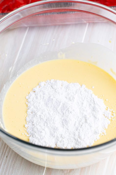 Powdered sugar being added to a cream cheese mixture in a bowl.