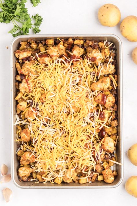 Bbq sauce and cheese added to potatoes and chicken on a sheet pan.