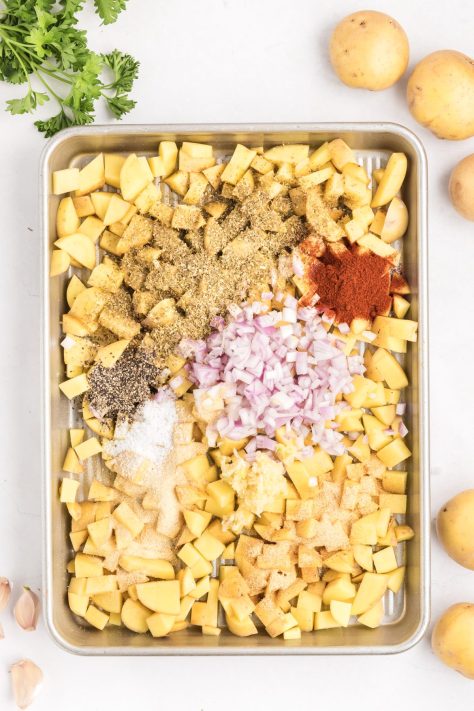 A baking sheet with potatoes, onions, and seasonings.