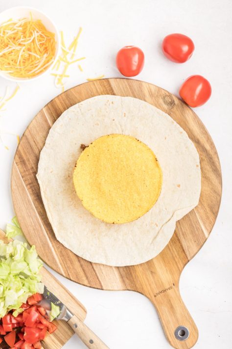 A tostada on top of meat and cheese mixture on a burrito shell.