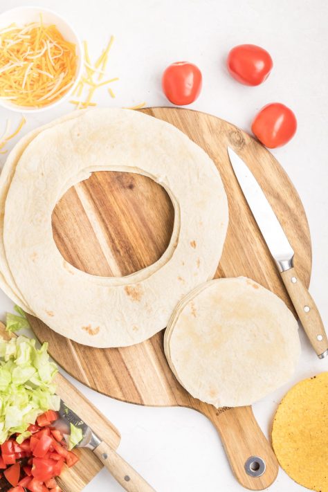 Burrito shells being cut into tostada sized circles.