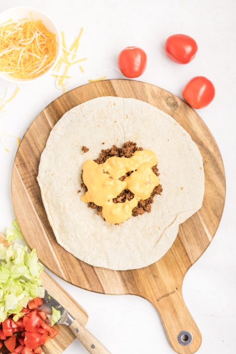 Queso being drizzled over beef mixture on a tortilla.