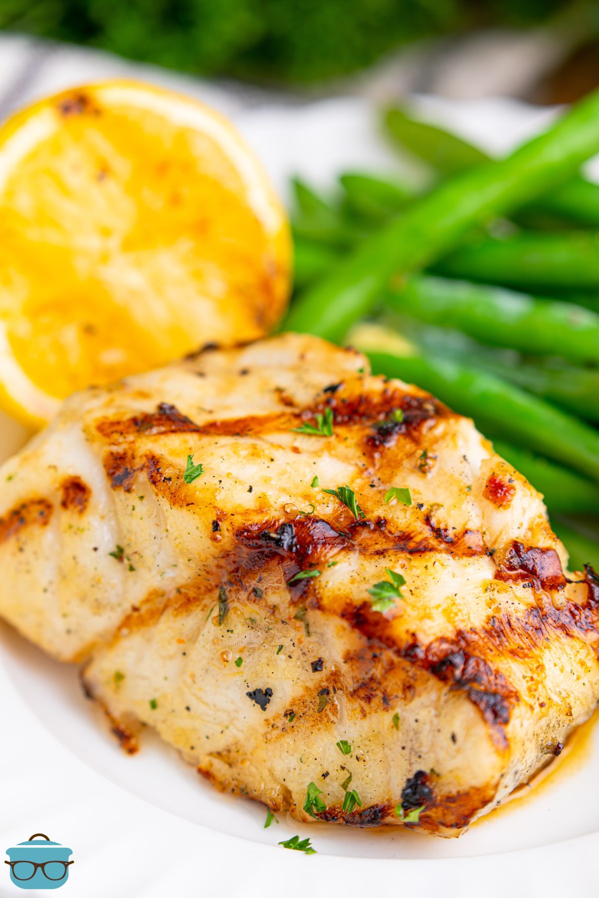 A piece of Grilled Sea Bass with lemon and green beans on a dinner plate.