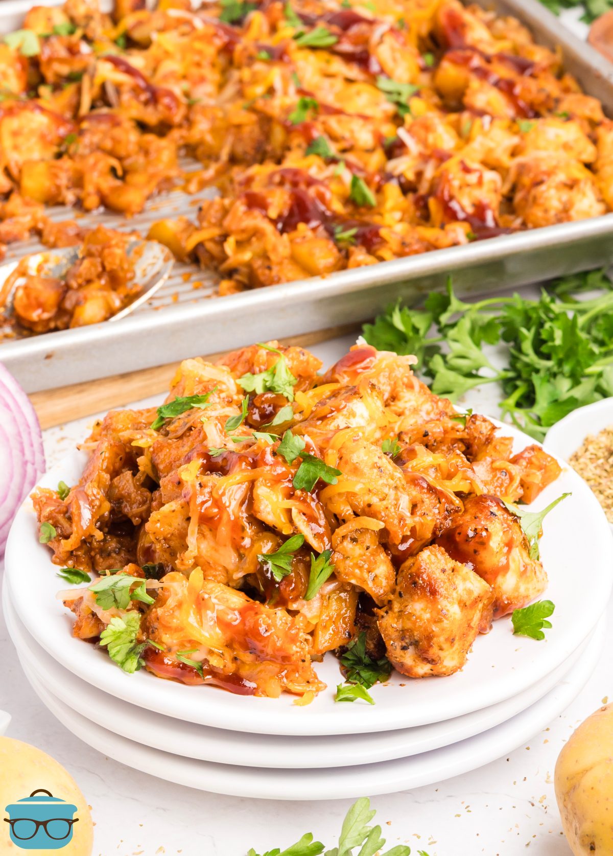 A stack of plates with a large serving of Sheet Pan BBQ Chicken and Potatoes next to the rest in the baking dish.