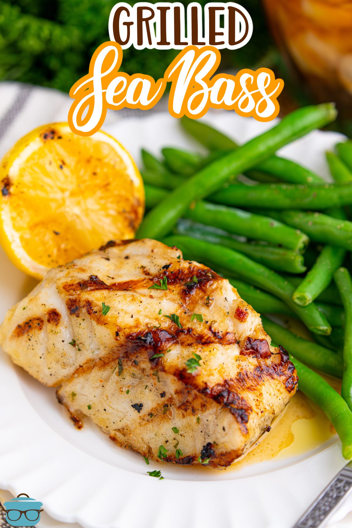 A plate with Grilled Sea Bass with green beans and a lemon wedge.